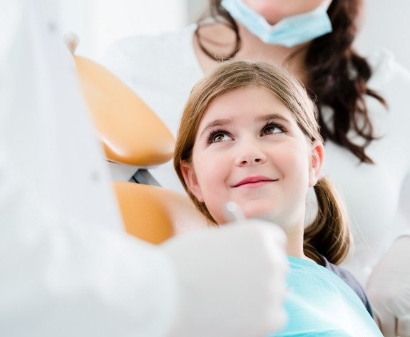 Young girl in dental chair looking up at her dentist