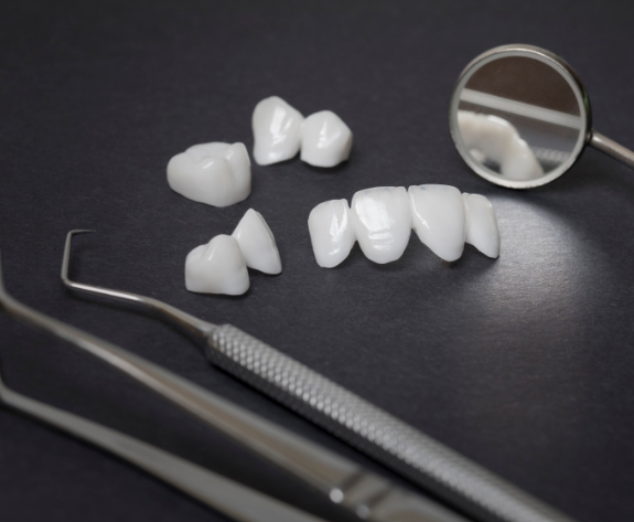 Several metal free dental crowns and veneers next to dental instruments on tray