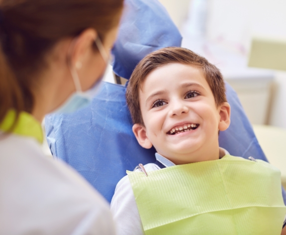 Young boy in dental chair smiling at his dentist