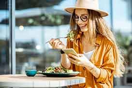 Woman smiling while looking at phone and eating lunch outside