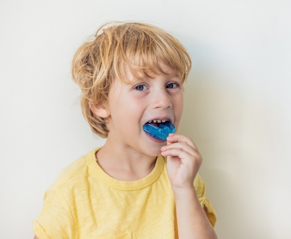 Young boy placing blue athletic mouthguard over his teeth