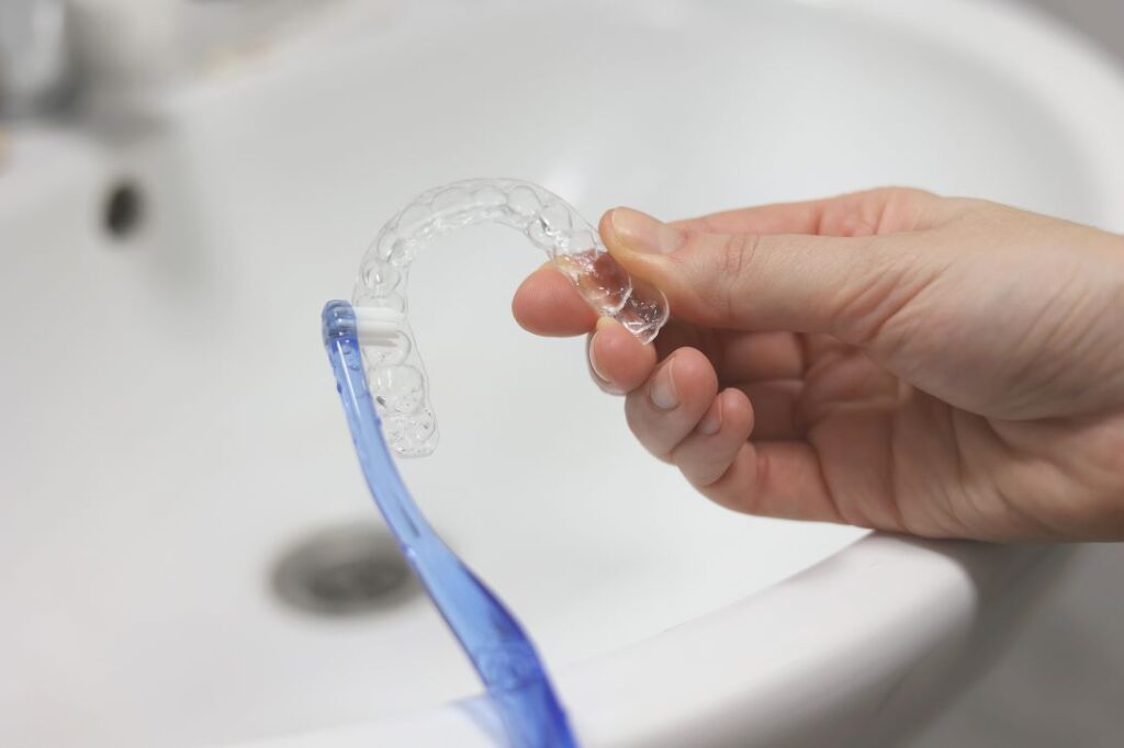 A person cleaning their Invisalign aligners with a toothbrush.