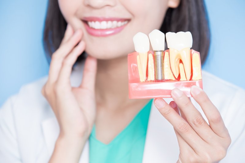 A blurred dentist holding an enlarged dental implant model